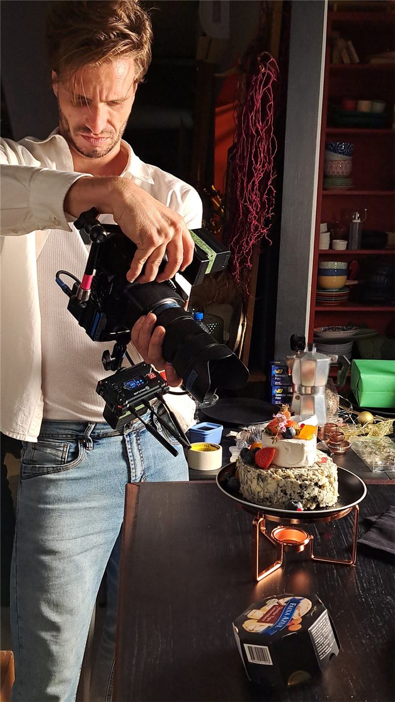 Thiago Maziero operando a câmera em set, fotografando um bolo de queijos